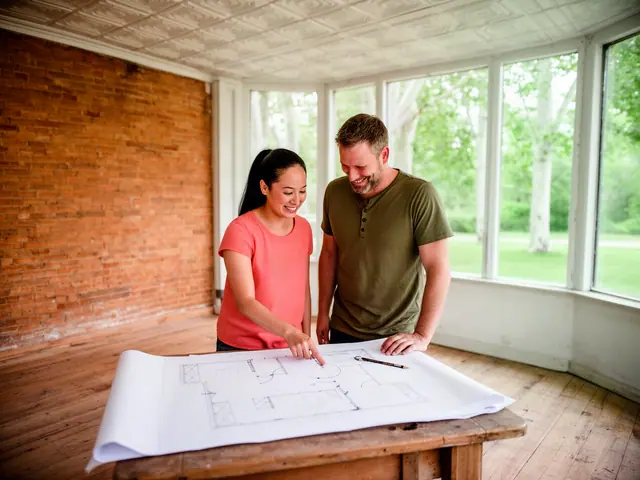 Two smiling partners reviewing a floor plan on a wooden table in an empty brick-walled room